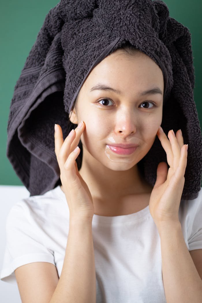 Woman applying fresh skincare with lip mask and towel wrap indoors.